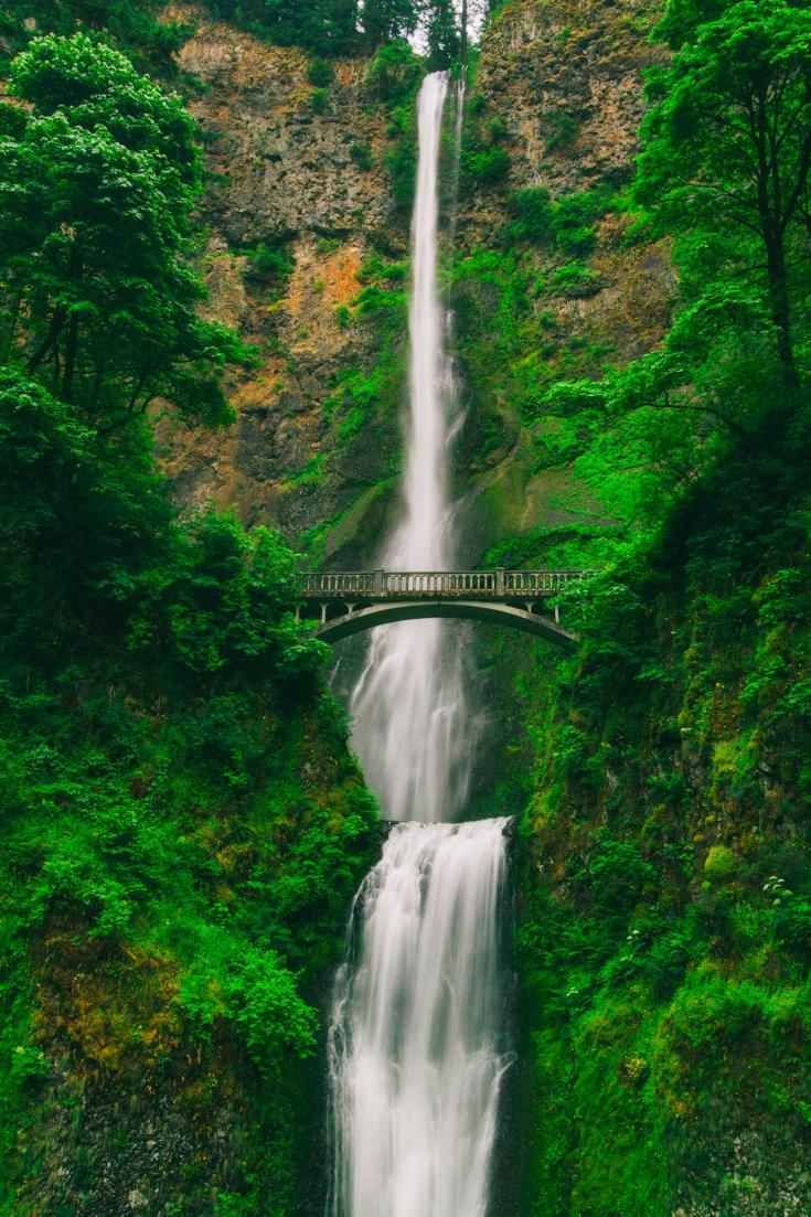 Bridge in front of a waterfall and green scenery